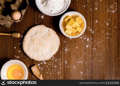 bread concept a bun dough, a tiny wooden spatula, a bowl of flour and a bowl of a raw egg organized on the wooden scene.