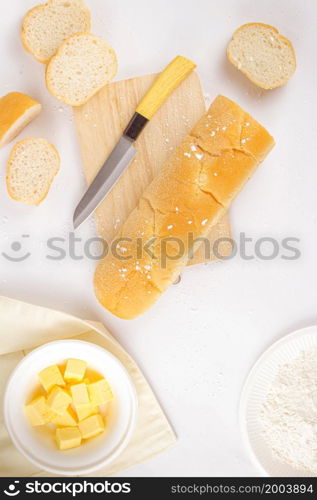 bread concept a loaf of bread, a few slices of bread, a knife, a wooden cutting board, and a bowl of butter lying on the white scene.