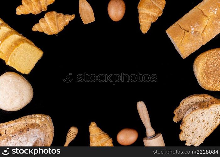 bread concept a small spatula, a rolling pin, an egg slices of bread, buns, croissants, and loaves of bread arranged in circle on the black background.