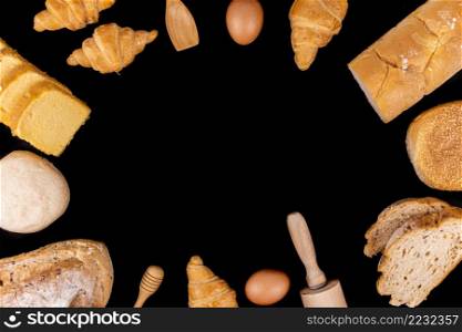 bread concept a small spatula, a rolling pin, an egg slices of bread, buns, croissants, and loaves of bread arranged in circle on the black background.