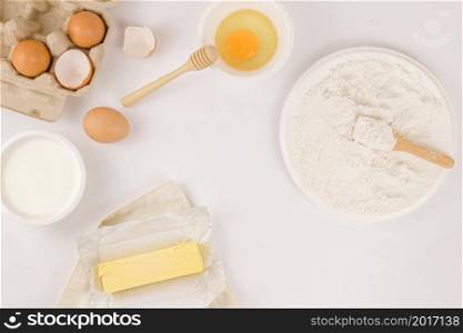 bread concept a stick of butter, a small bowl of raw egg, a plate of flour with a wooden spatula on it being on the light background.