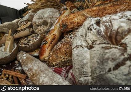 Bread concept. Brown and white whole grain loaves wrapped in kraft paper composition on rustic dark wood with wheat ears scattered around. Baking and home bread making concept. Soft toning