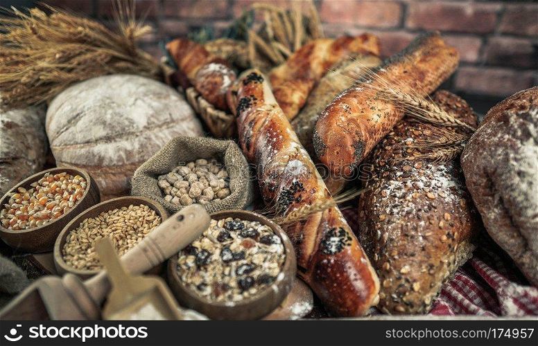 Bread concept. Brown and white whole grain loaves wrapped in kraft paper composition on rustic dark wood with wheat ears scattered around. Baking and home bread making concept. Soft toning