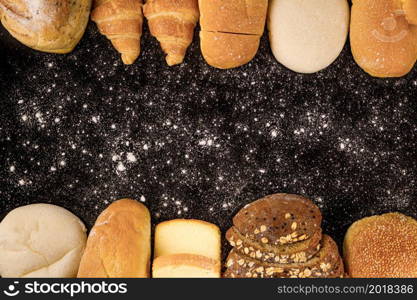 bread concept loaves of bread, buns, slices of bread with seeds, and croissants arranged on the dark background with icy sprinkling on it.