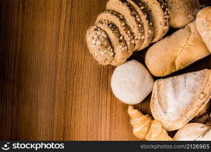 bread concept several slices of dark brown bread with seeds, buns, croissants, and loaves of bread gathered together on the wooden background.