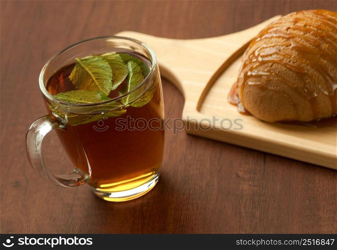 bread drizzled with honey on a wooden plate and a glass of black tea with leaf. bread on a wooden plate and a glass of tea