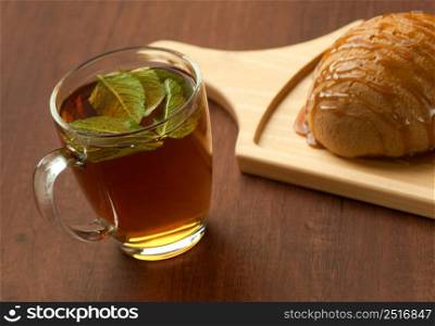 bread drizzled with honey on a wooden plate and a glass of black tea with leaf. bread on a wooden plate and a glass of tea