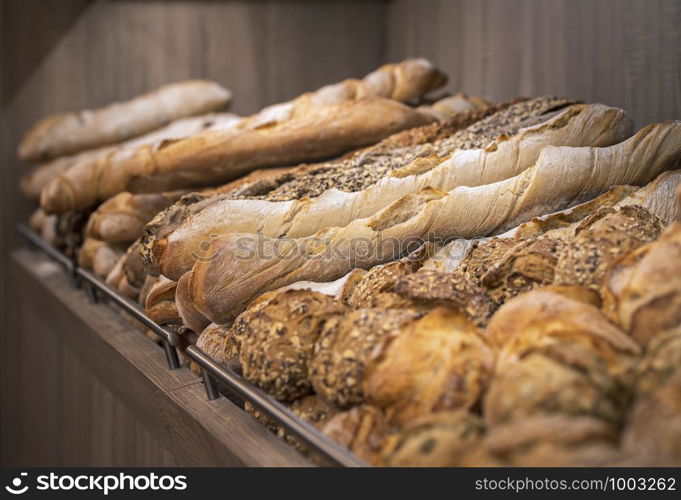 Bread mix on wooden shelves. Bakery goods displayed on a shelf. Various types of loaves. Freshly baked crusty breads. Appetizing french bread.