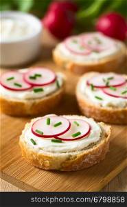 Bread slices with cream cheese, radish slices and chives on wooden board, photographed with natural light (Selective Focus, Focus on the front of the radish slices on the first bread)