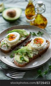 Bread toast, boiled eggs, avocado slice, microgreens on a plate, breakfast time