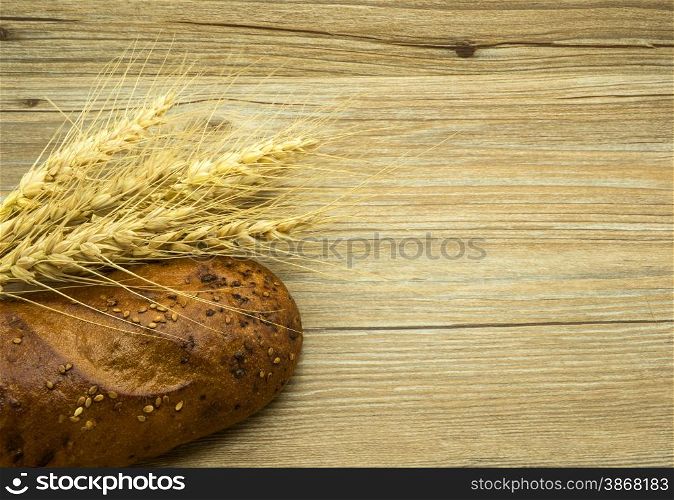 Bread with sesame seeds and ears on a wooden background.