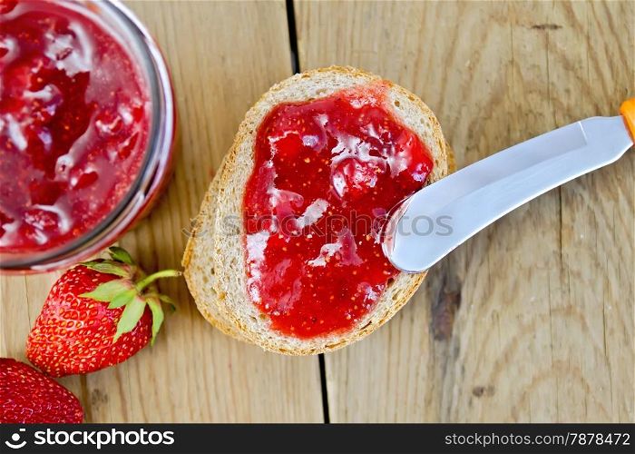 Bread with strawberry jam, a jar of jam, knife, strawberries on the background of the old wooden boards