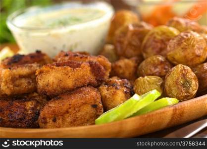 Breaded fried calamary pieces with small baked potatoes and tzatziki (Selective Focus, Focus on the front of the upper calamary and the first potato on the right of the image)