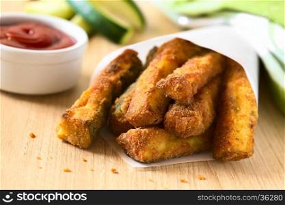 Breaded fried zucchini sticks in paper cone with ketchup in the back, photographed with natural light (Selective Focus, Focus on the front of the upper zucchini sticks)