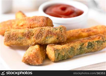 Breaded fried zucchini sticks with ketchup in the back, photographed with natural light (Selective Focus, Focus in the middle of the image)