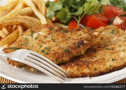 breaded homemade chicken schnitzels or escalopes with french fries and a tomato and green salad
