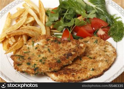 breaded homemade chicken schnitzels or escalopes with french fries and a tomato and green salad