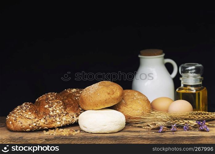 Breads, milk and oil on wood table with black background.