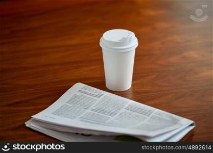 break, mass media and news concept - coffee drink in paper cup and newspaper on table