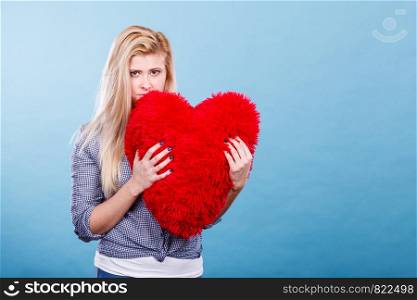 Break up, divorce, bad relationship concept. Sad, depressed woman holding big red fluffy pillow in heart shape, she needs love.. Sad woman holding red pillow in heart shape