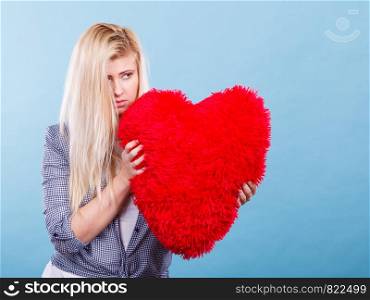Break up, divorce, bad relationship concept. Sad, depressed woman holding big red fluffy pillow in heart shape, she needs love.. Sad woman holding red pillow in heart shape