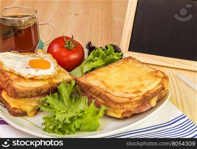 Breakfast and chalkboard on wooden table - Quick snack with ham and cheese sandwiches, cup of tea, tomato and fresh salad. Beside the plate with food is a blackboard and chalk for writing messages.