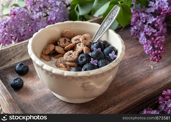 Breakfast cereals with yogurt, blueberries and lilac flowers on a tray