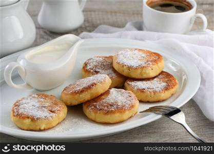Breakfast. Cheese pancakes with sour cream sprinkled with powdered sugar on a white plate.