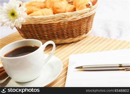Breakfast coffee and croissants on a light background with a notebook for notes on the table.