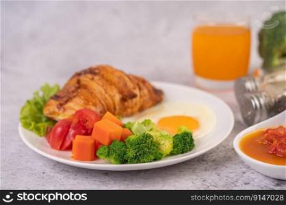 Breakfast consisting of bread, fried eggs, broccoli, carrots, tomatoes and lettuce on a white plate