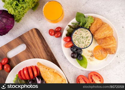 Breakfast consists of croissant, fried egg, salad dressing, black grapes, and tomatoes.