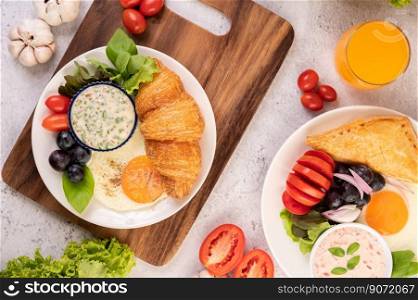 Breakfast consists of croissant, fried egg, salad dressing, black grapes, and tomatoes.