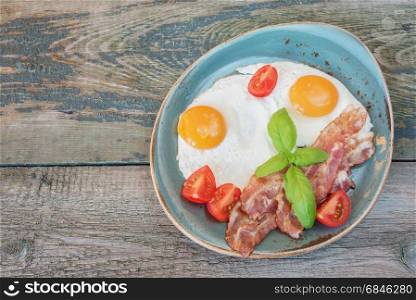 Breakfast consists of fried eggs, bacon, tomato on the old wooden table, with space for text