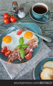 Breakfast consists of fried eggs, bacon, tomato, toast and a cup of coffee on the old wooden table, vertical image