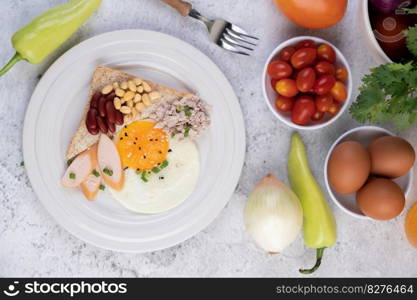 Breakfast consists of fried eggs, sausage, minced pork, bread, red beans and soy on a white plate.