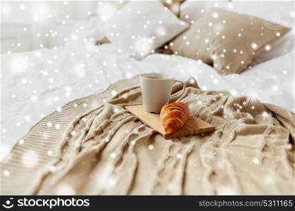 breakfast, cosy home and morning concept - cozy bedroom with coffee cup and croissant on wooden board in bed over snow. coffee cup and croissant on plaid in bed at home