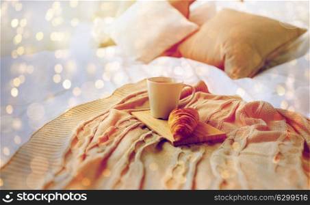 breakfast, coziness, morning, holidays and winter concept - cozy bedroom with coffee cup and croissant on wooden board in bed at home. coffee cup and croissant on plaid in bed at home