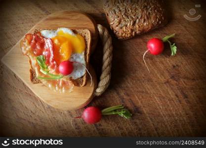 Breakfast , crispy bacon, fried eggs and bread. Sandwich on cutting board. Rustic table . Top view .. Breakfast , crispy bacon, fried eggs and bread. Sandwich on cutting board. Rustic table . Top view