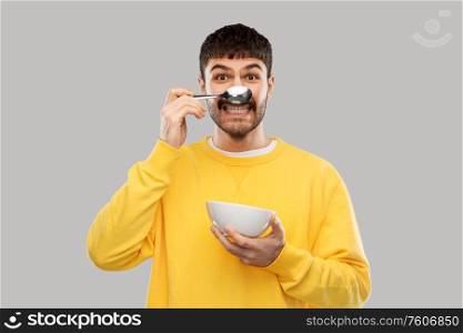 breakfast, eating and people concept - happy smiling young man with spoon and bowl having fun over grey background. smiling young man with spoon and bowl having fun