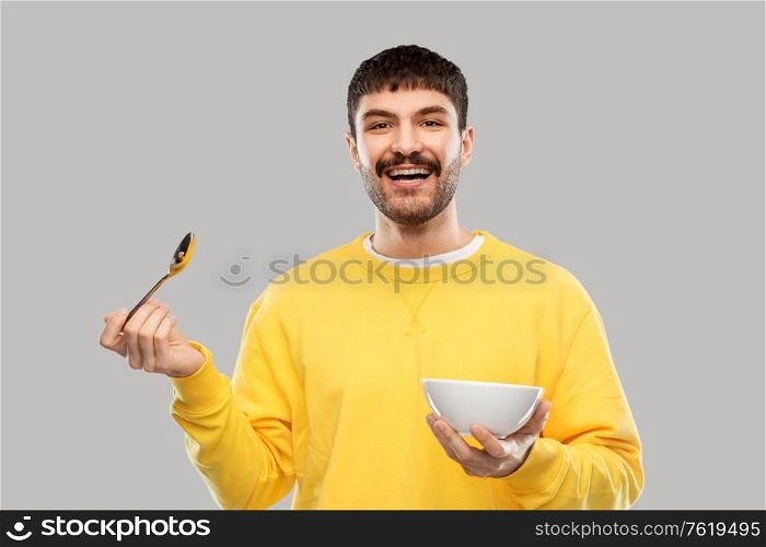 breakfast, eating and people concept - happy smiling young man with spoon and bowl over grey background. smiling young man with spoon and bowl eating