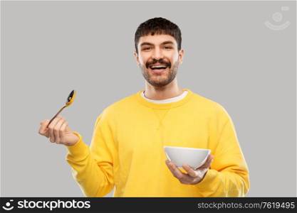 breakfast, eating and people concept - happy smiling young man with spoon and bowl over grey background. smiling young man with spoon and bowl eating