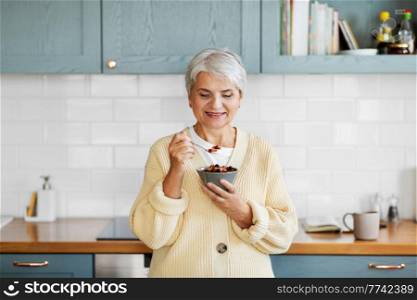 breakfast, food and people concept - happy smiling woman with spoon eating cereal on kitchen at home. woman with cereal for breakfast on kitchen at home