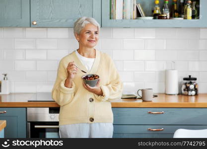 breakfast, food and people concept - happy smiling woman with spoon eating cereal on kitchen at home. woman with cereal for breakfast on kitchen at home