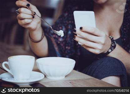 breakfast - girl sitting with smartphone and a cup of coffee and dessert
