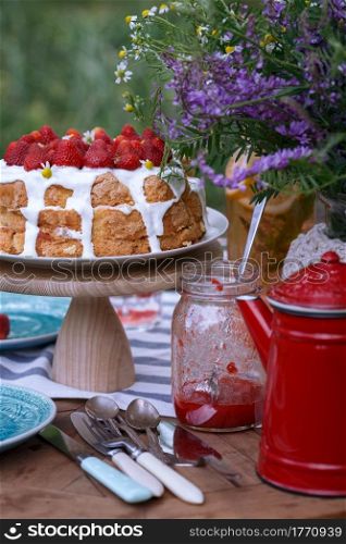 breakfast in the garden. on the table is a vase of flowers, cake with strawberries and glasses of lemonade