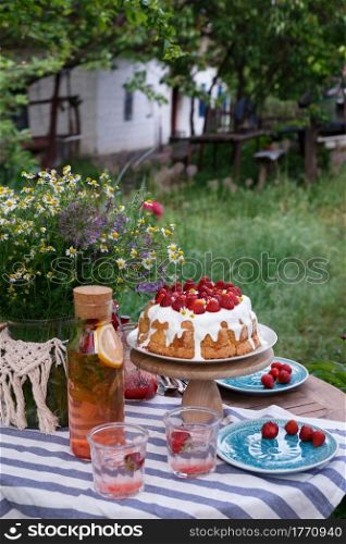 breakfast in the garden. on the table is a vase of flowers, cake with strawberries and glasses of lemonade
