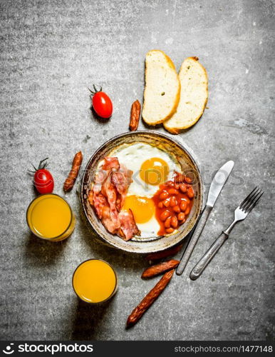 Breakfast in the morning. Bacon, fried eggs with beans and orange juice. On the stone table.. Bacon, fried eggs with beans and orange juice.