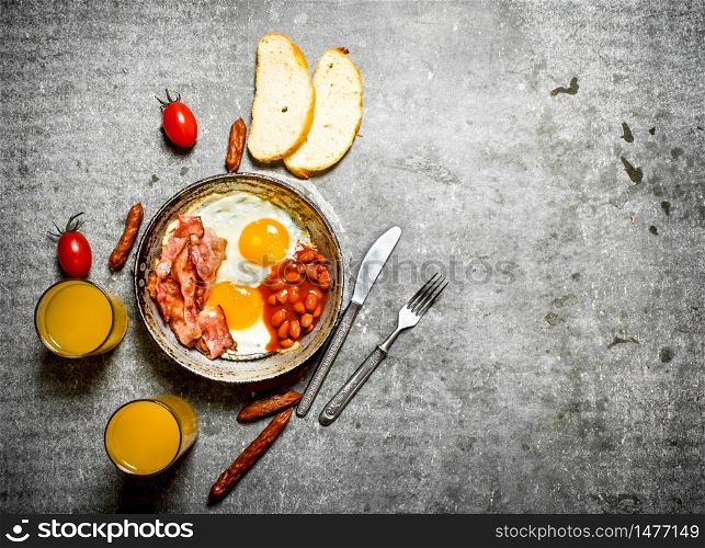 Breakfast in the morning. Bacon, fried eggs with beans and orange juice. On the stone table.. Bacon, fried eggs with beans and orange juice.