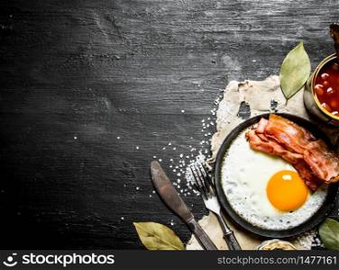 Breakfast in the morning. Beans with fried egg and bacon. On a black wooden background.. Breakfast in the morning. Beans with fried egg and bacon.