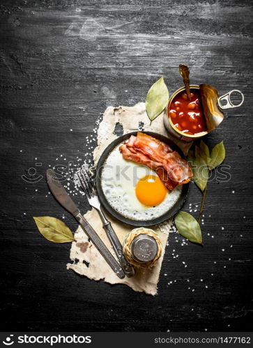 Breakfast in the morning. Beans with fried egg and bacon. On a black wooden background.. Breakfast in the morning. Beans with fried egg and bacon.